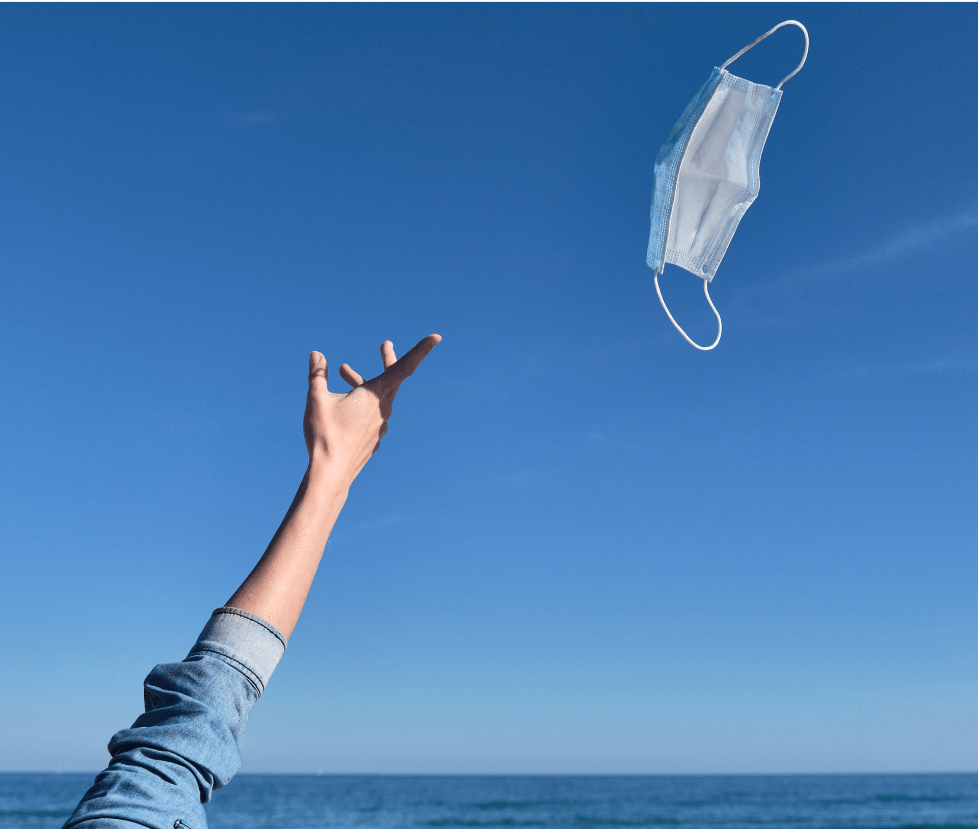 Hand throwing a mask in the air as a sign of freedom after receiving the vaccine, end of the pandemic, mask-free holidays, end of covid-19, normal life post-pandemic, virus-free summer