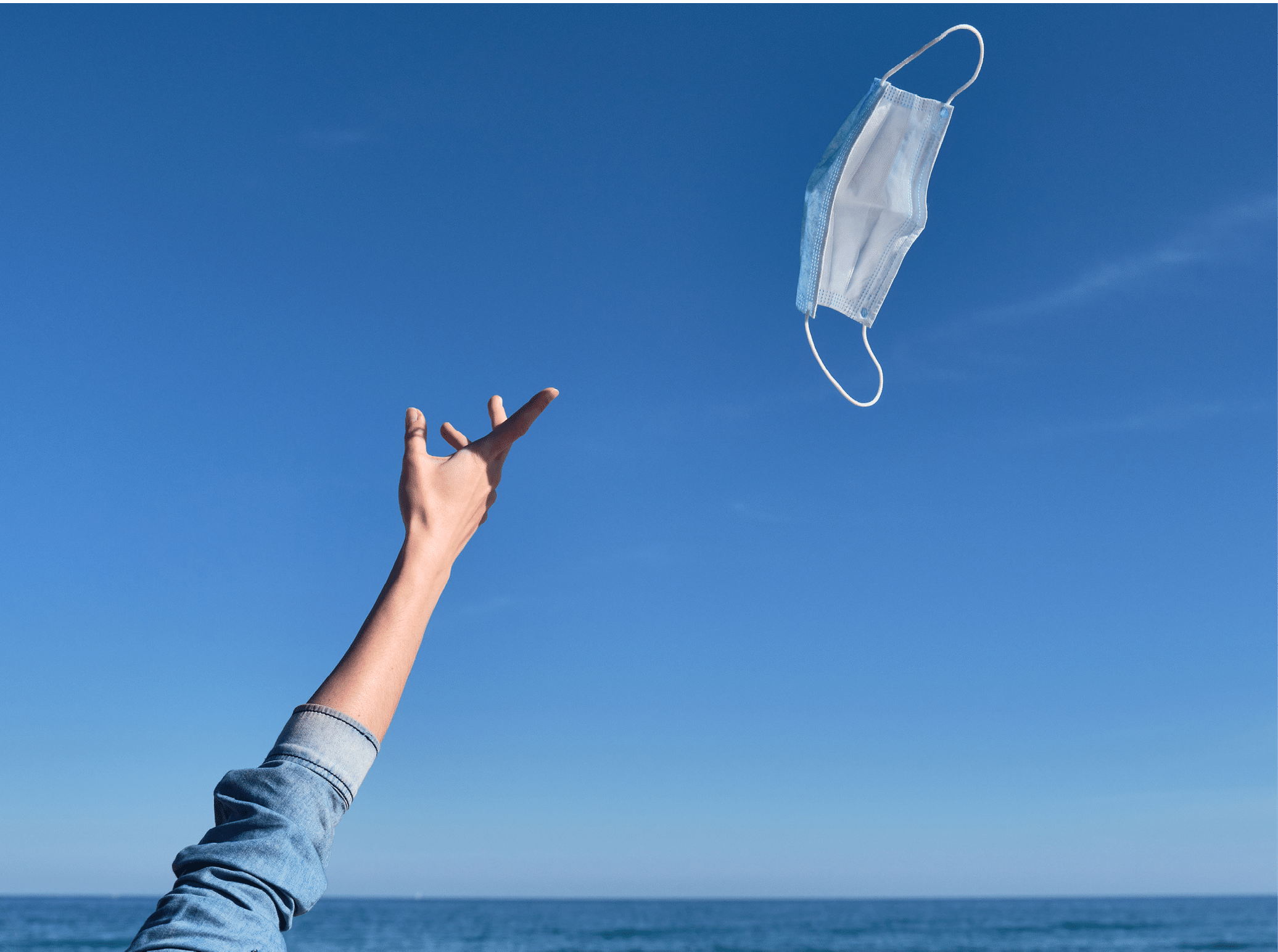 Hand throwing a mask in the air as a sign of freedom after receiving the vaccine, end of the pandemic, mask-free holidays, end of covid-19, normal life post-pandemic, virus-free summer